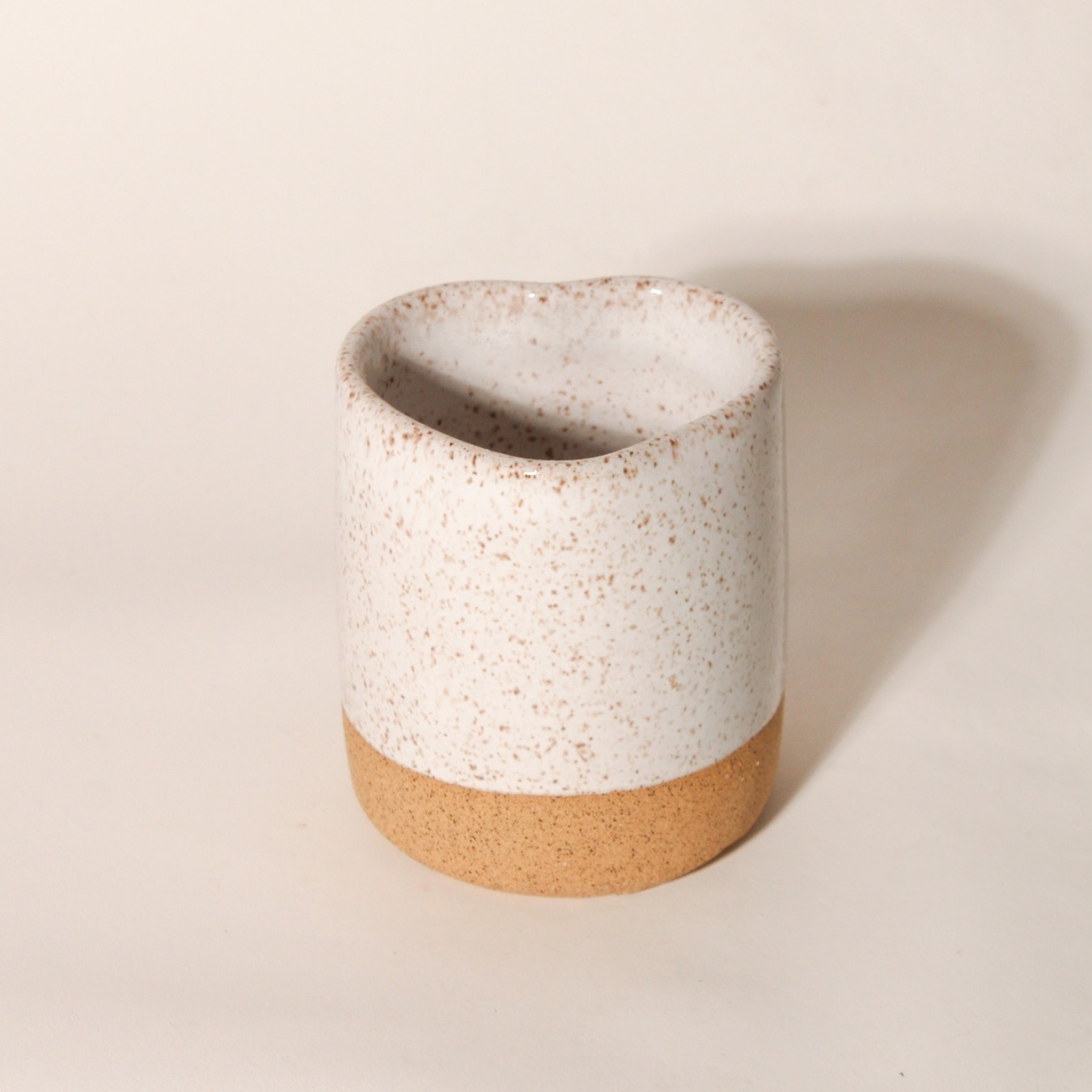 Copo Coração de cerâmica, com a base em argila natural e topo em esmalte branco salpicado, em fundo neutro Esmo