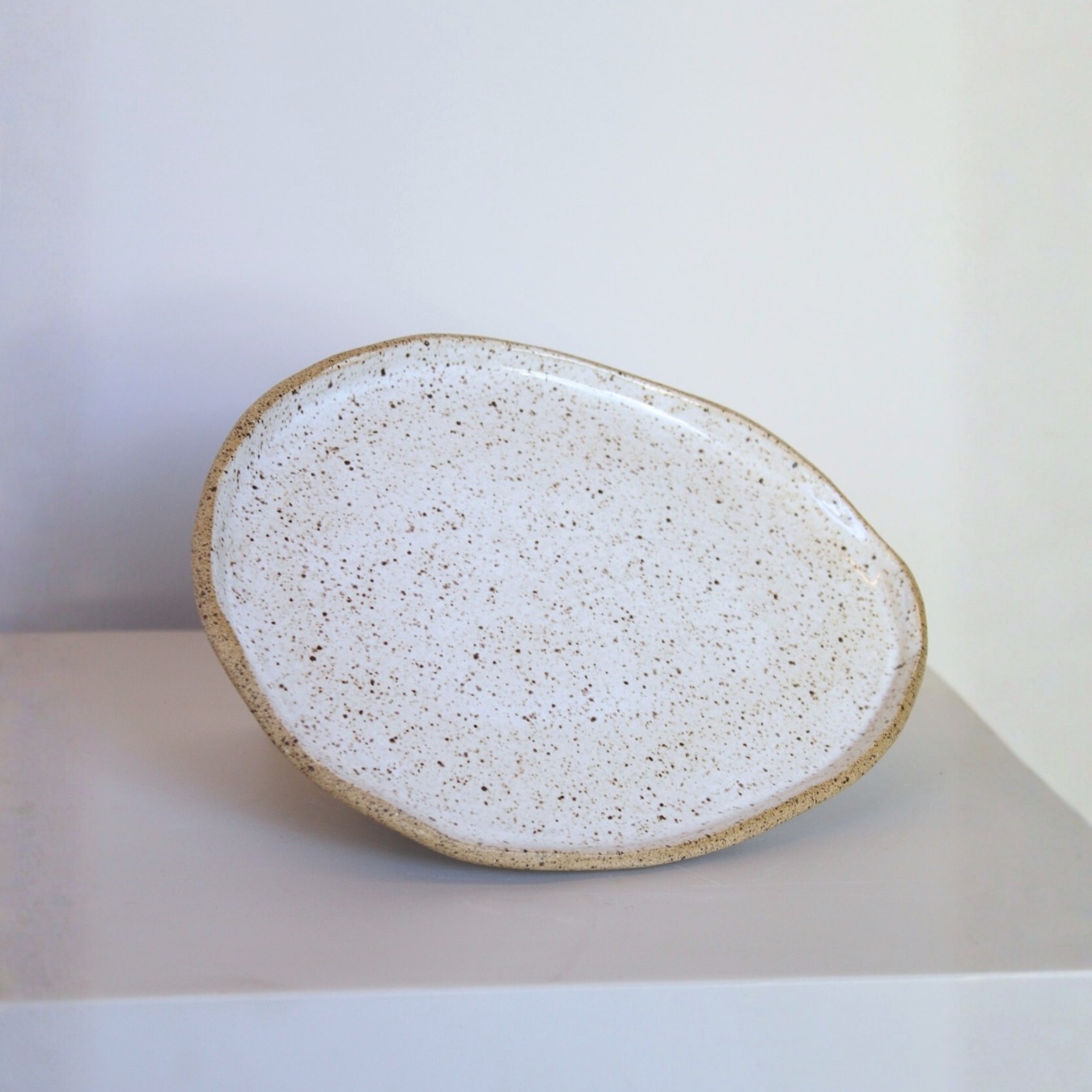Prato Oval de cerâmica Esmo na cor branca salpicada, com borda em argila tabaco aparente.