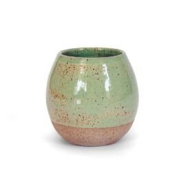 Copo Esmo de cerâmica na cor Pistache. A peça possui formato abaulado, com a parte superior revestida por um esmalte verde suave e brilhante contendo pequenos pontilhados orgânicos, e a parte inferior preservando a textura rústica e opaca da argila natural. O fundo da imagem é branco.