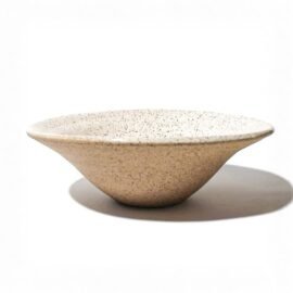 Fruteira Esmo em cerâmica na versão Off-White, com formato cônico e superfície fosca de textura orgânica e pontilhada, projetando uma sombra bem delineada sob luz direcional.