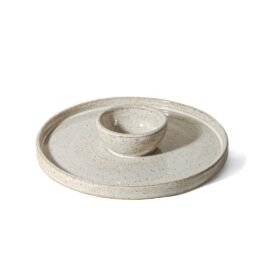 Petisqueira circular de cerâmica com bowl central integrado, na cor Off-White de acabamento mate. A superfície apresenta textura sutil com pequenos pontos da argila tabaco, fotografada em ângulo superior contra um fundo branco.