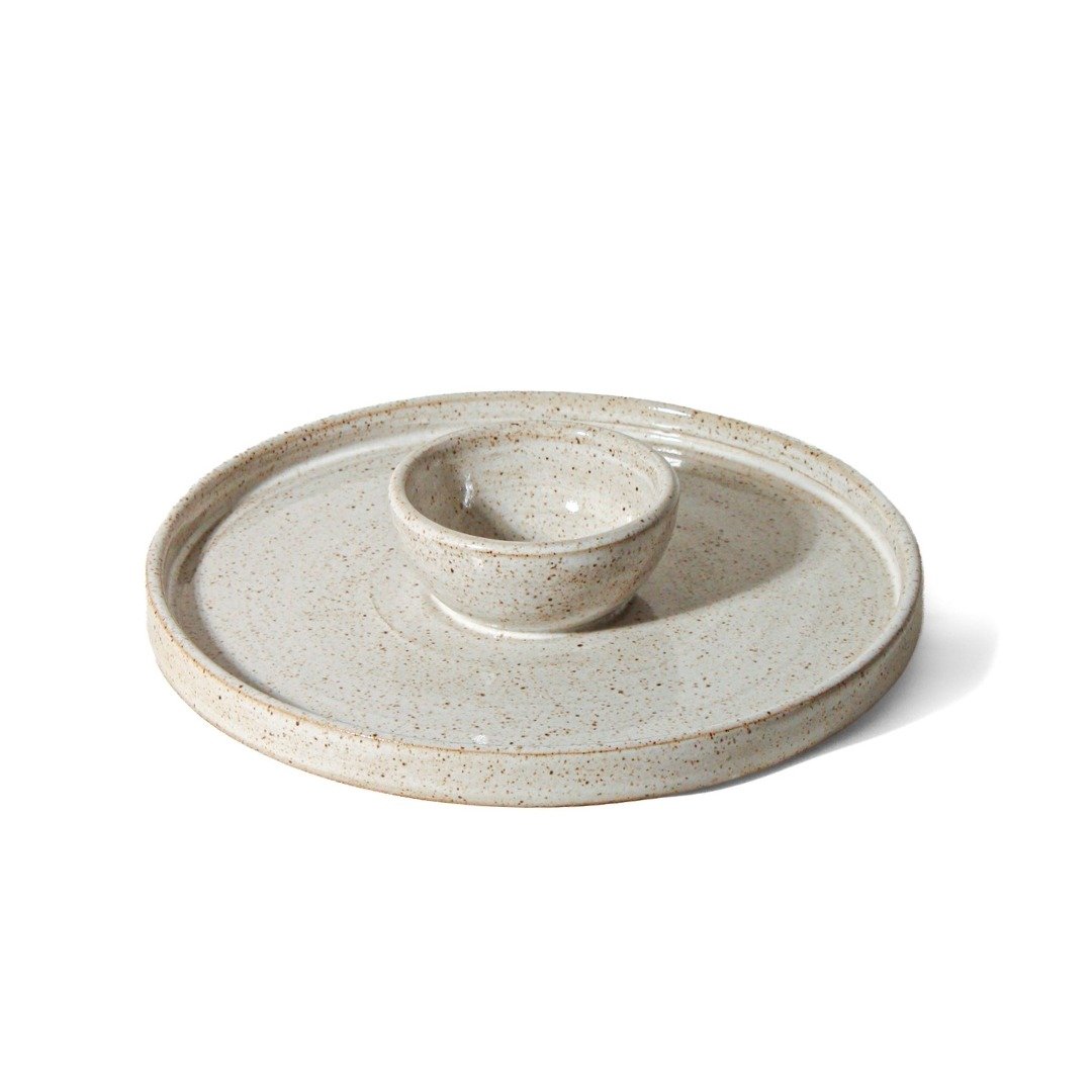 Petisqueira circular de cerâmica com bowl central integrado, na cor Off-White de acabamento mate. A superfície apresenta textura sutil com pequenos pontos da argila tabaco, fotografada em ângulo superior contra um fundo branco.