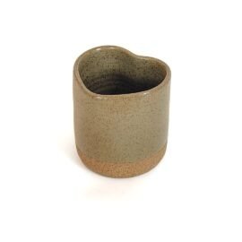 Copo Coração em cerâmica na cor Oliva. Peça com formato ergonômico de coração, apresentando um esmalte verde sóbrio acetinado com denso pontilhado orgânico na parte superior e base em argila rústica aparente.
