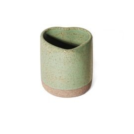 Copo de cerâmica em formato orgânico de coração na cor Pistache da Esmo Cerâmica. A peça apresenta um nítido contraste visual e tátil: a base é feita em cerâmica crua rústica, enquanto o corpo superior recebe um esmalte vitrificado verde suave, repleto de um pontilhado orgânico natural da massa.
