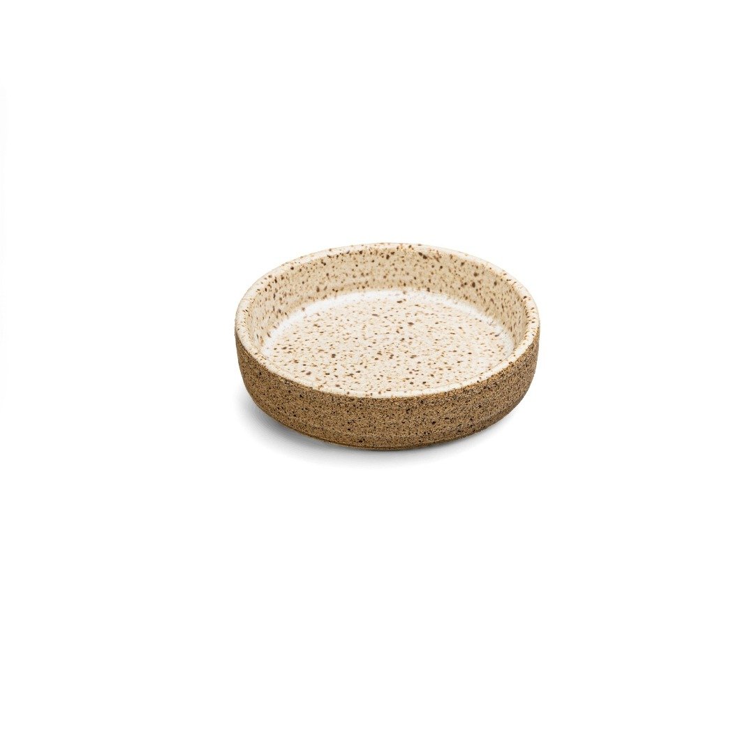 Porta-Shoyu redondo e raso de cerâmica artesanl da Esmo Cerâmica, visto em ângulo sobre fundo branco. A borda e a superfície interna possuem esmalte na cor Off-White, com acabamento mate e sutis pontinhos escuros salpicados. A parede externa exibe a textura rústica, granulada e porosa da argila tabaco natural em tom terroso.