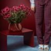 Centro de Mesa Alto Grande da Esmo Cerâmica na cor Borgonha repleto de flores rosas, ambientado sobre uma mesa vermelha de design moderno.