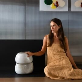 A designer e fundadora da Esmo, Bruna Vuelma, ao lado de dois Centros de Mesa Alto empilhados, demonstrando a volumetria imponente, a ergonomia visual e a proporção das peças em cerâmica texturizada.