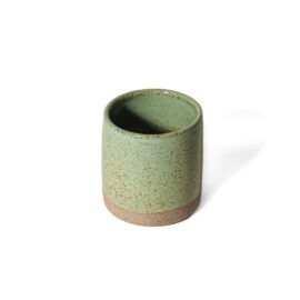 Copo Reto para tomar Café Expresso de cerâmica na cor Pistache da Esmo. A peça de formato cilíndrico e tamanho reduzido possui acabamento superior em esmalte verde suave vitrificado, com finos pontilhados naturais escuros. A faixa da base inferior revela a textura rústica e opaca da argila crua.