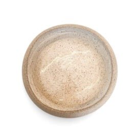 Vista superior do Prato Inverso da Esmo em sua posição côncava, voltada para o ato de servir. O centro rebaixado apresenta um esmalte acetinado luminoso na cor Off-White, salpicado por minúsculas pontuações terrosas. A silhueta perfeitamente orgânica é delimitada pela borda cru em cerâmica artesanal sem esmalte, evidenciando o design minimalista, a pureza formal e o encontro táctil dos materiais sob luz suave.
