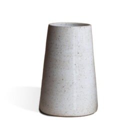 Vaso Cônico Grande na cor Off-White da Esmo. A peça decorativa em cerâmica artesanal possui silhueta geométrica de linhas retas, afunilando em direção ao topo. O acabamento mate revela uma textura orgânica com sutis pontilhados escuros, difundindo a luz suavemente pela superfície. Na base ampla, observa-se um fino filete de cerâmica rústica escura aparente, gerando um elegante contraste visual e projetando uma leve sombra à esquerda sobre um fundo claro.