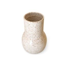 Vaso Gota Pequeno na cor Off-White, uma peça de cerâmica artesanal da Esmo. A imagem destaca a silhueta geométrica em proporção compacta, com uma base arredondada e volumosa que se afunila perfeitamente para um gargalo rigorosamente reto. A luz incide de maneira suave sobre o acabamento acetinado e mate, evidenciando a textura orgânica com leves pontilhados naturais ao longo da superfície clara. A iluminação cria um sutil jogo de sombras na base curva, ressaltando a pureza formal, o aspecto tátil e o minimalismo que caracterizam o design do objeto.