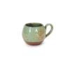Xícara Esmo Expresso em cerâmica na cor Pistache. A peça apresenta um forte contraste visual e tátil entre a parte superior de silhueta arredondada, esmaltada em verde suave com acabamento vitrificado e pontilhado natural, e a base rústica em cerâmica cru exposta.