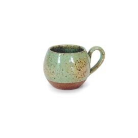 Xícara Esmo Expresso em cerâmica na cor Pistache. A peça apresenta um forte contraste visual e tátil entre a parte superior de silhueta arredondada, esmaltada em verde suave com acabamento vitrificado e pontilhado natural, e a base rústica em cerâmica cru exposta.